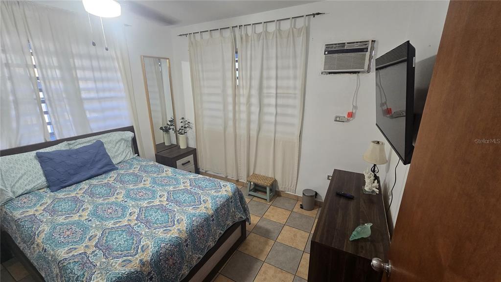 A bedroom features a bed with a patterned quilt, tiled floors, and a wall-mounted television — 3 WILLIAM FONT STREET, CULEBRA, PR