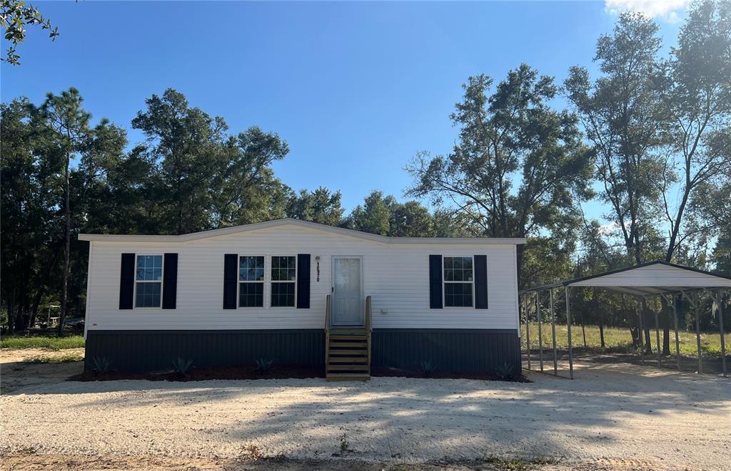 A single-story manufactured home with white siding, dark shutters, and an attached metal carport — 10970 NE 109TH STREET, ARCHER, FL