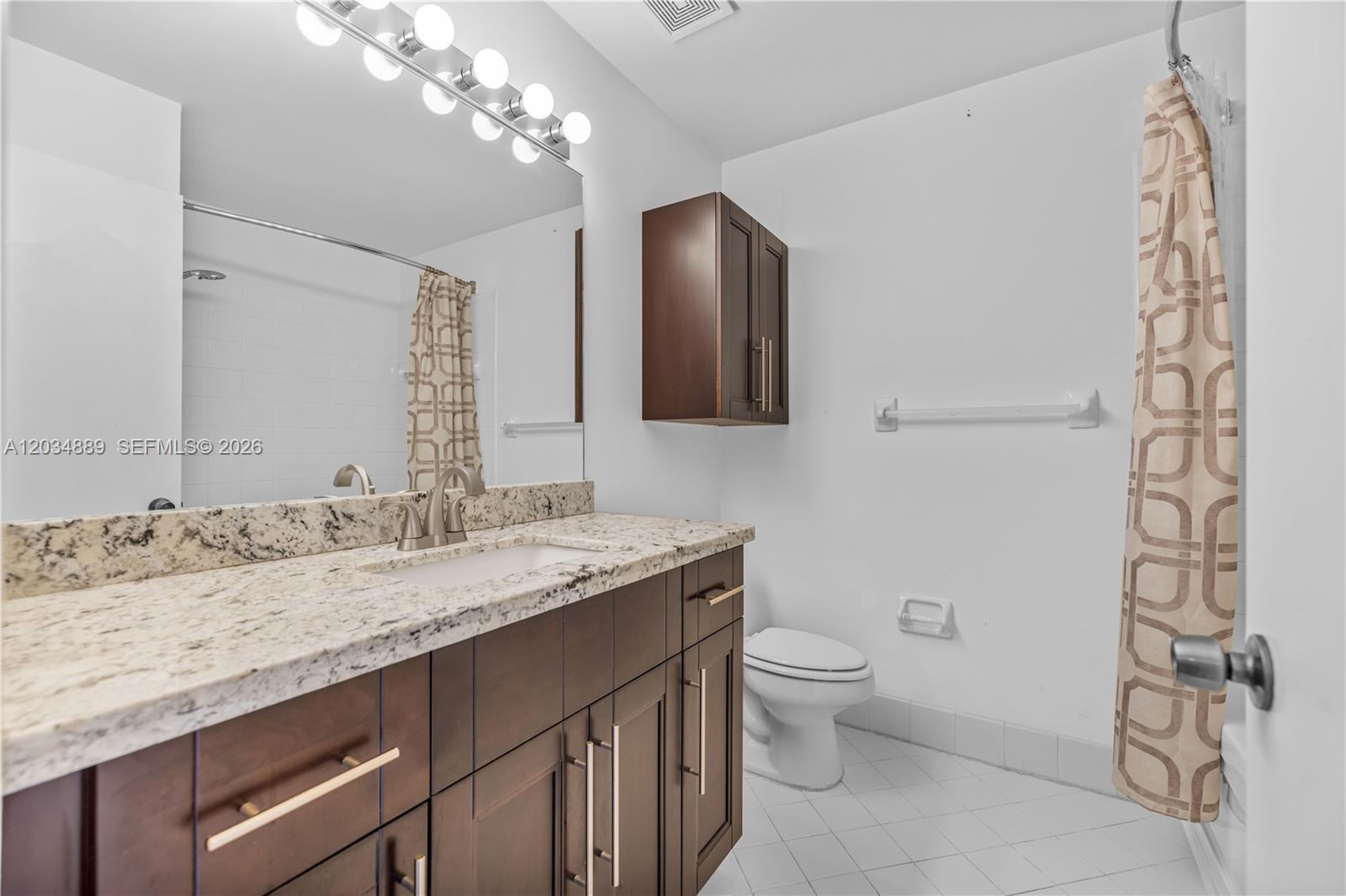 A bathroom features a dark wood vanity with a granite countertop and a wall cabinet — 1125 SW 44th Ave, Deerfield Beach FL 33442, DEERFIELD BEACH, FL