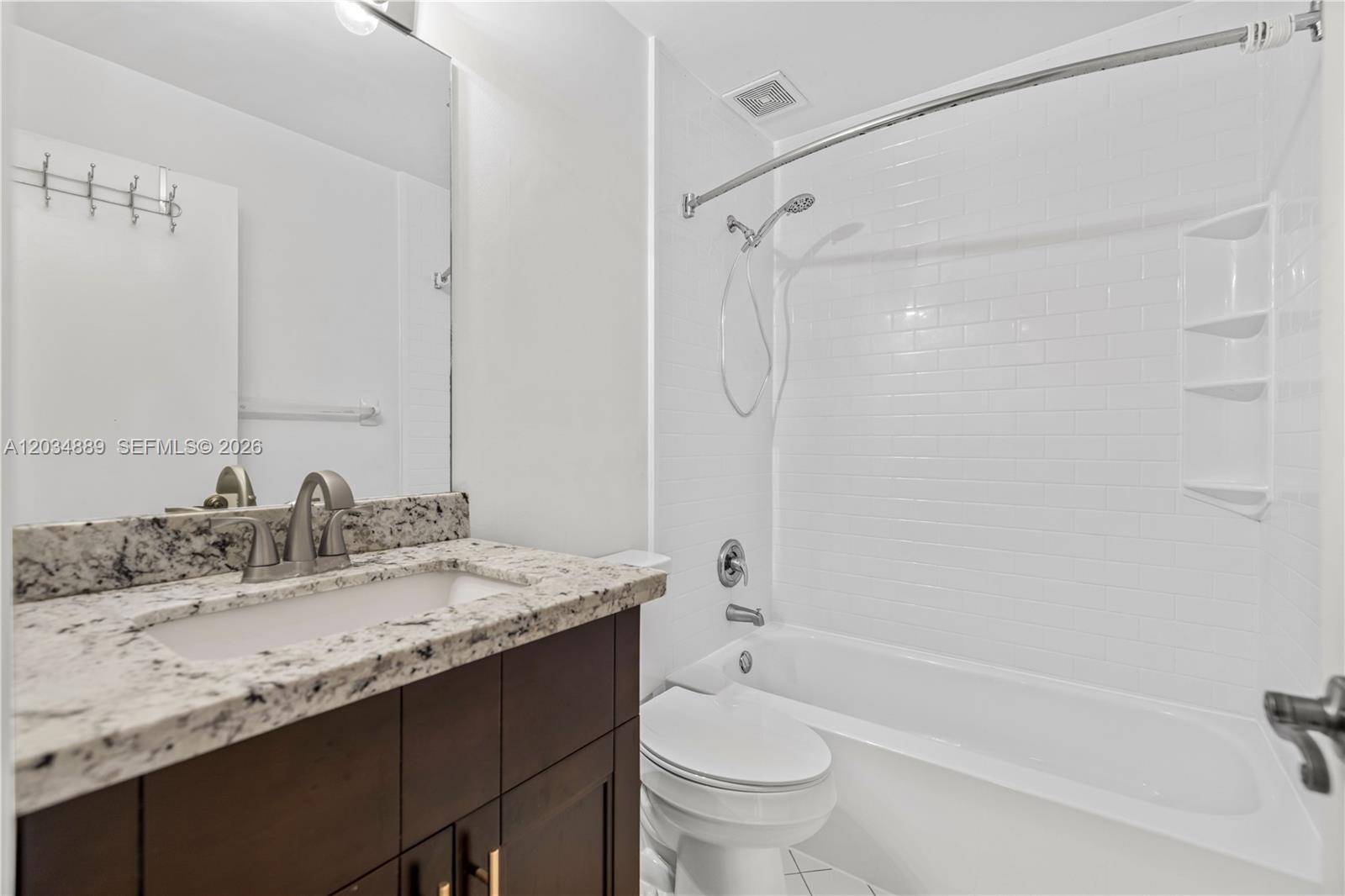 A bathroom features a dark wood vanity with granite countertop, toilet, and white tiled tub — 1125 SW 44th Ave, Deerfield Beach FL 33442, DEERFIELD BEACH, FL