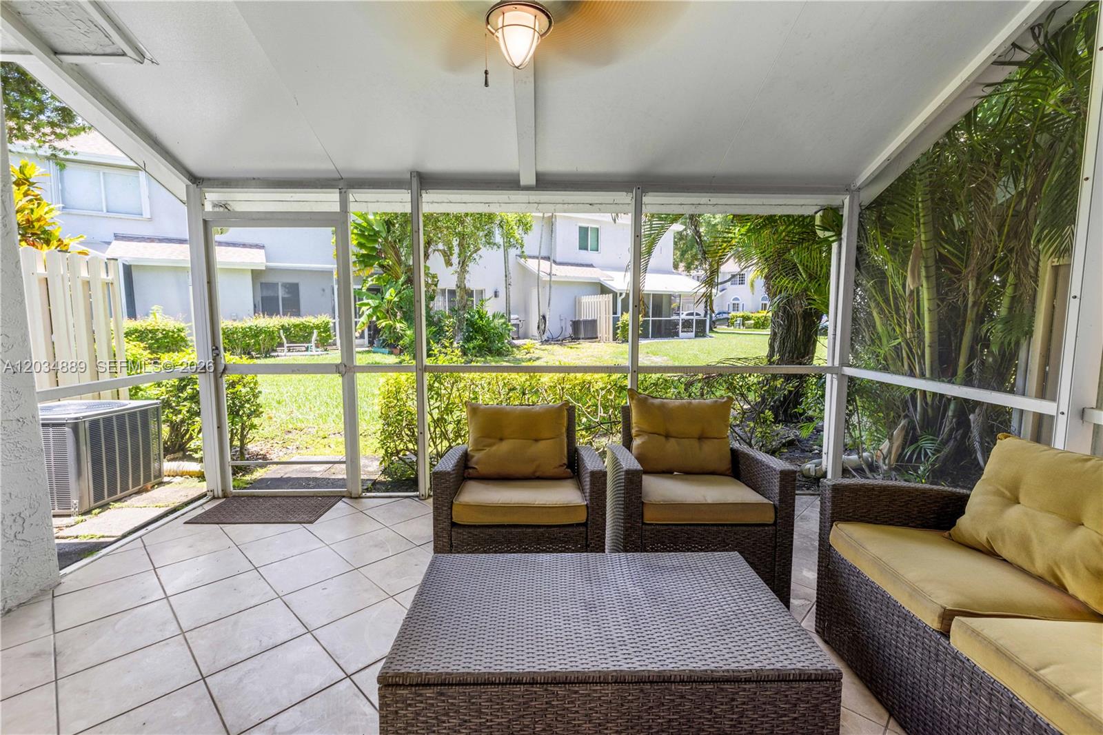 A screened-in patio features tiled flooring, wicker furniture, and a view of a grassy yard — 1125 SW 44th Ave, Deerfield Beach FL 33442, DEERFIELD BEACH, FL