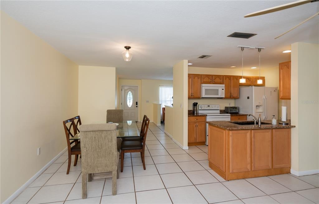 A dining area with a glass table sits adjacent to a kitchen with wood cabinets — 23258 MIDWAY BLVD, PORT CHARLOTTE, FL