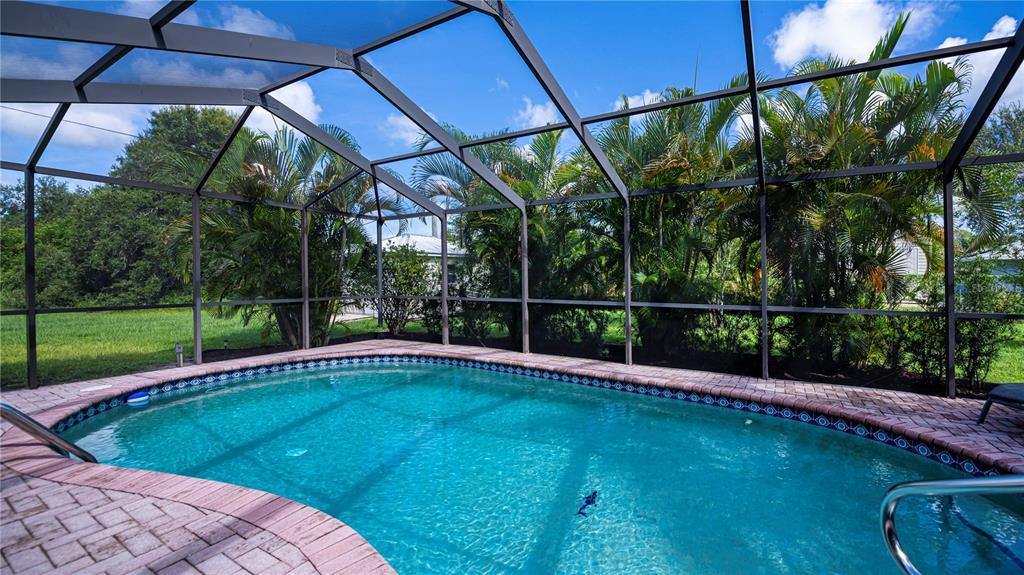A swimming pool with a brick deck is enclosed by a screened lanai structure — 23258 MIDWAY BLVD, PORT CHARLOTTE, FL