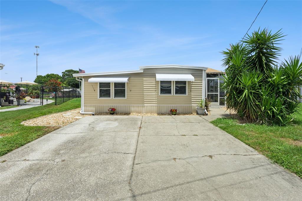 A single-story manufactured home with beige siding, a concrete driveway, and a large palm tree — 30127 GREEN BAY DRIVE, TAVARES, FL