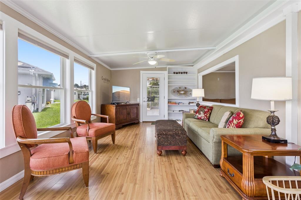 A sunroom features light wood flooring, a green sofa, two orange chairs, and a ceiling fan — 30127 GREEN BAY DRIVE, TAVARES, FL