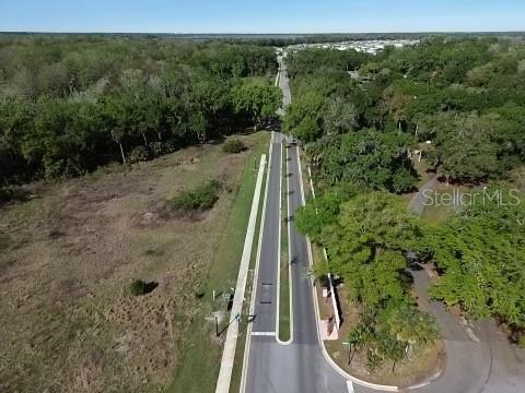 An aerial view shows a paved road leading through a wooded area toward a neighborhood — 29994 ANAHID DRIVE, LEESBURG, FL
