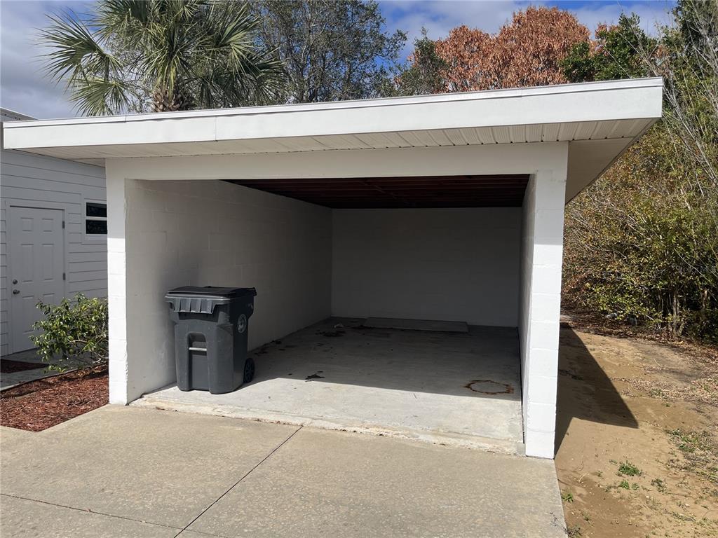 A white concrete block carport with a flat roof and a trash bin inside — 930 W MAIN STREET, AVON PARK, FL