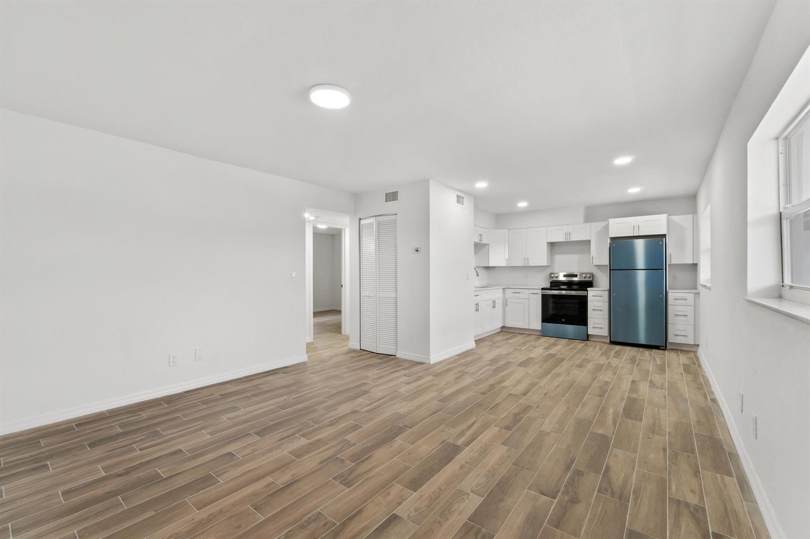 An open-concept kitchen and living area features white cabinets, stainless steel appliances, and wood-look flooring — 1301 Emerald Terrace # 4, Fort Pierce FL 34950, FORT PIERCE, FL