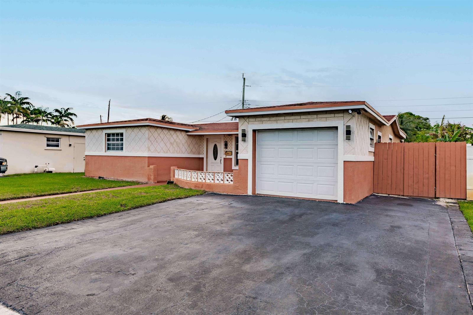 A single-story house with a peach stucco exterior, a white garage door, and a driveway — LAUDERDALE LAKES, FL
