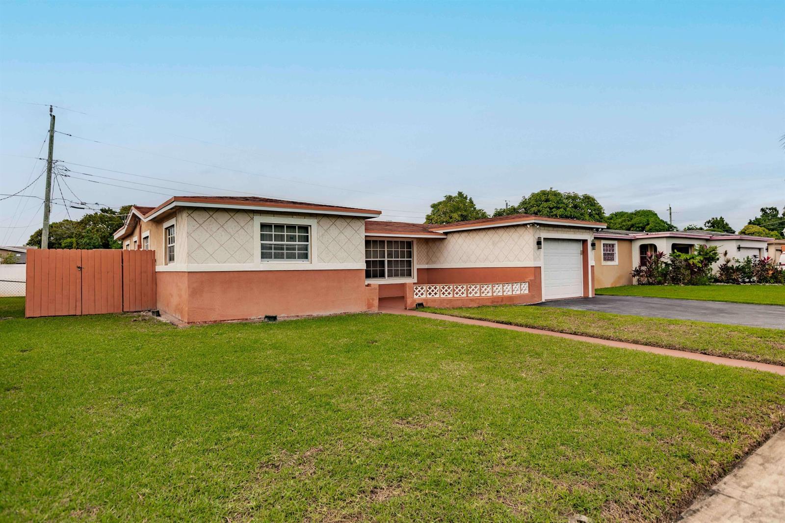 A single-story house with a peach-colored exterior, a garage, and a fenced-in side yard — LAUDERDALE LAKES, FL