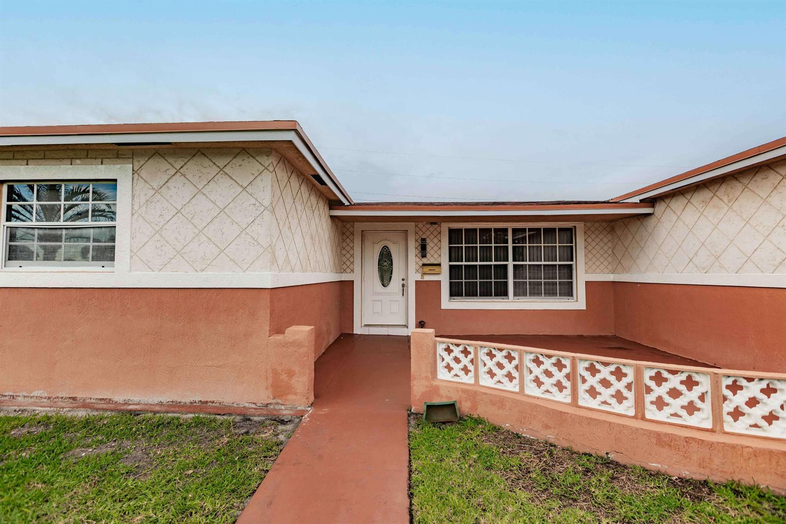 The exterior of a single-story house features a terracotta-colored base, textured walls, and a porch — LAUDERDALE LAKES, FL