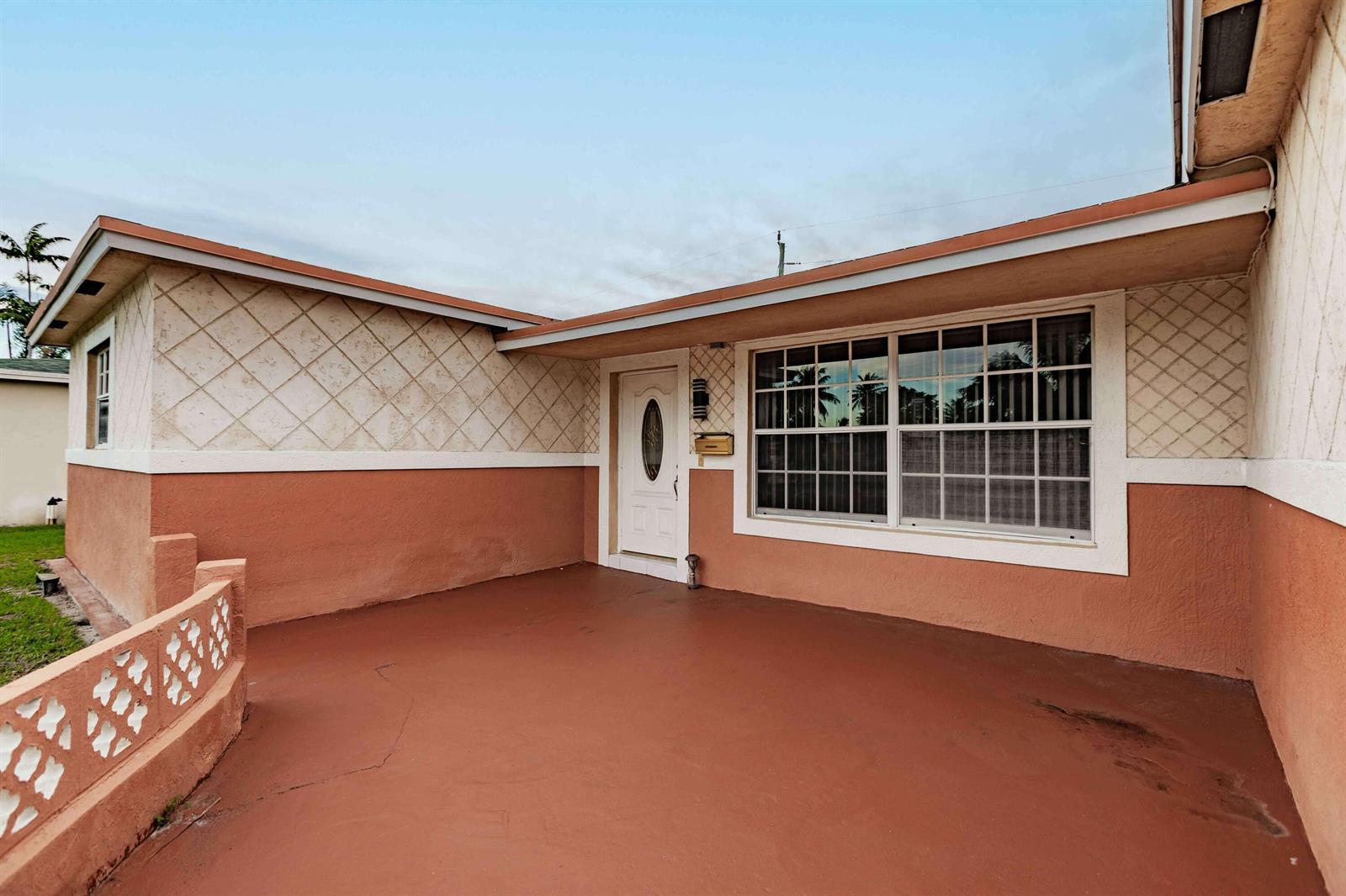 The exterior of a house features a terracotta-colored porch, a white front door, and lattice-patterned walls — LAUDERDALE LAKES, FL