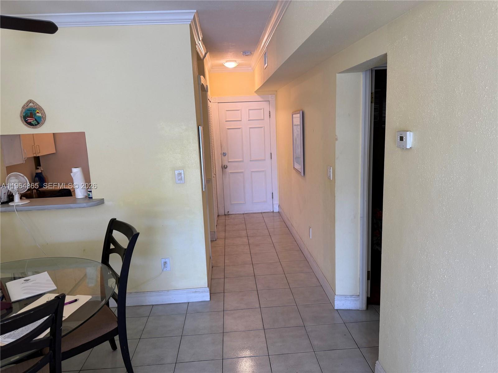 A dining area with a glass table leads to a hallway with a white door — 2500 Diana Dr # 107, Hallandale Beach FL 33009, HALLANDALE BEACH, FL