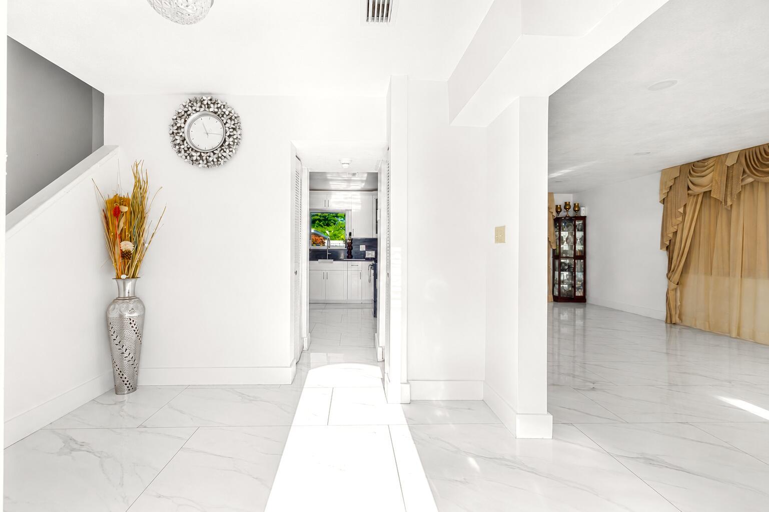 A bright entryway with white marble floors, a decorative wall clock, and a tall vase — 3111 Thames Way, Miramar FL 33025, MIRAMAR, FL
