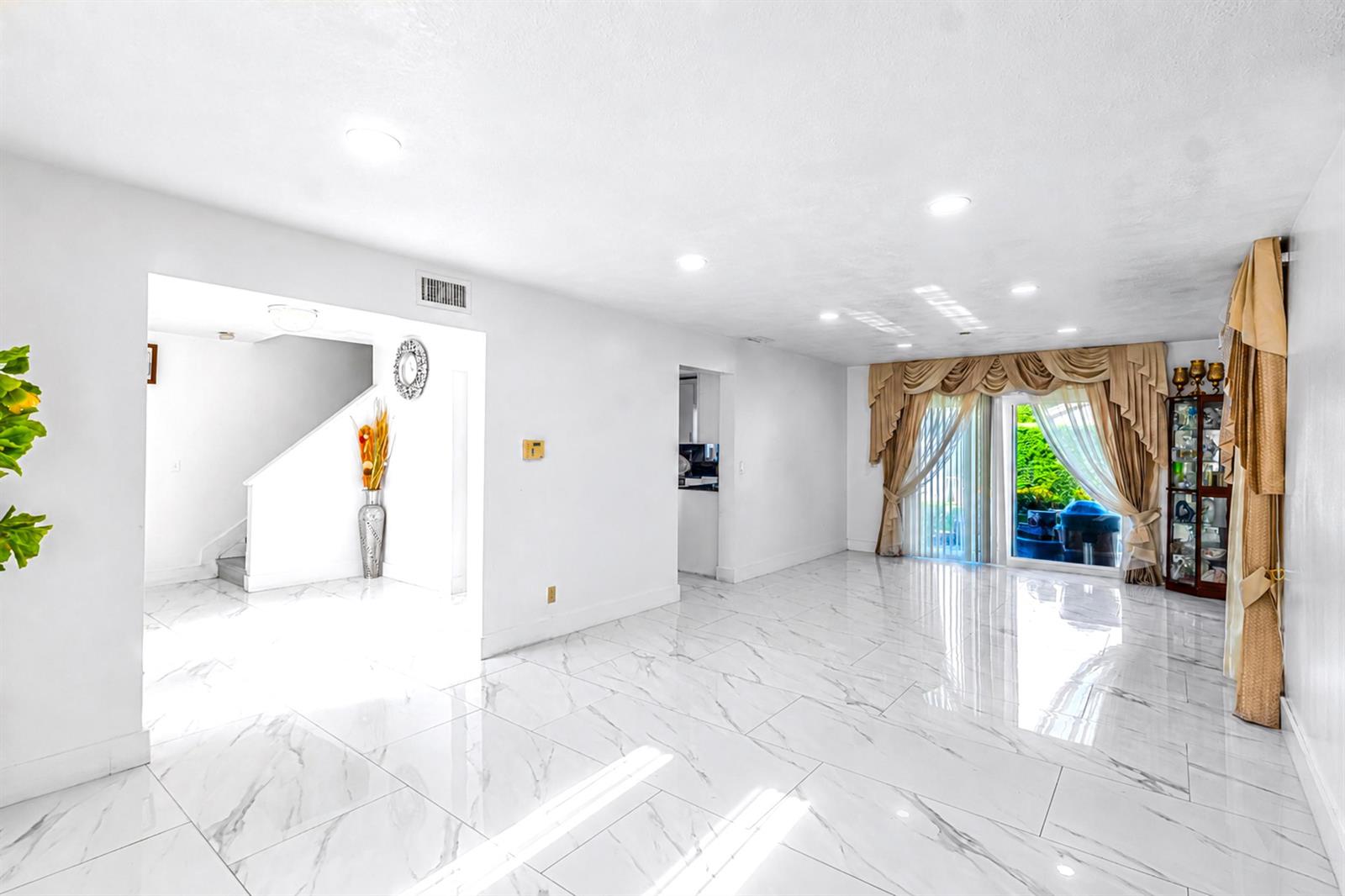 A bright living room features white marble-look tile flooring, recessed lighting, and large sliding glass doors — 3111 Thames Way, Miramar FL 33025, MIRAMAR, FL