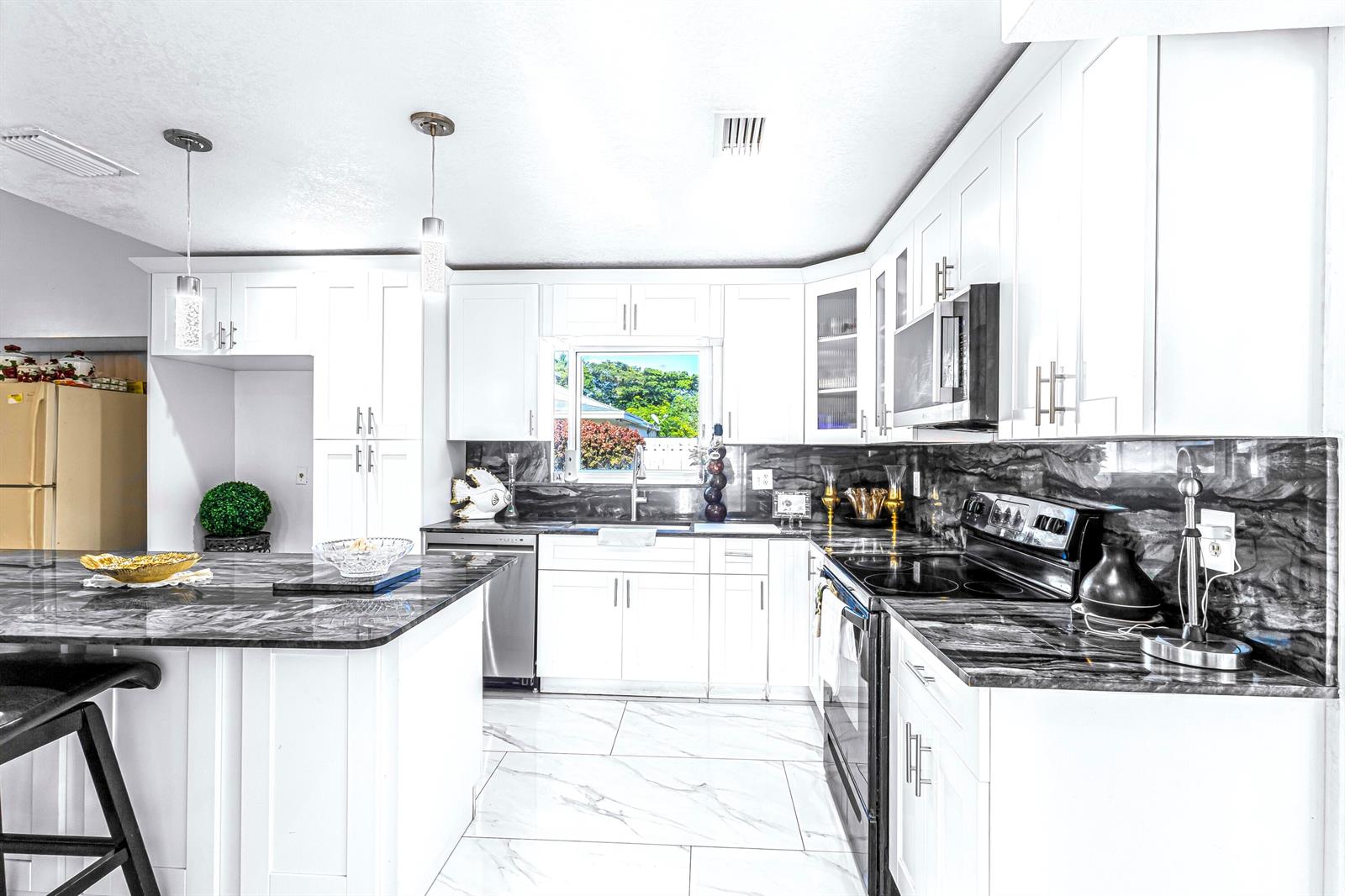 A kitchen features white cabinets, dark marble-patterned countertops, and light-colored tile flooring — 3111 Thames Way, Miramar FL 33025, MIRAMAR, FL