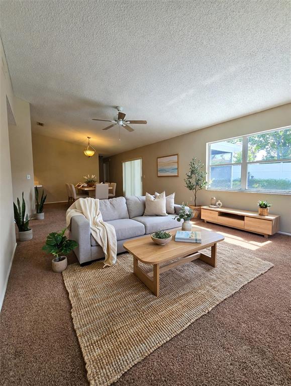 A spacious living room features beige carpeting, a ceiling fan, and a sliding glass door — 9836 MOREHEAD LANE, PORT RICHEY, FL
