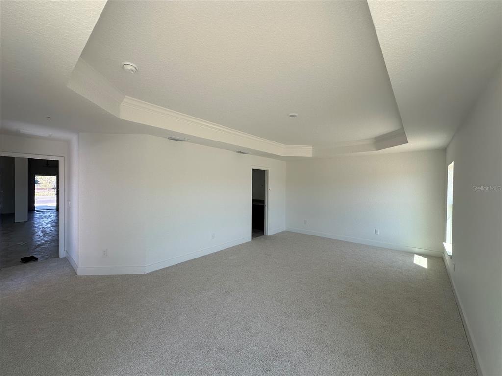 An empty bedroom features a tray ceiling, beige carpet, and white walls — 12555 NE 48TH TERR, OXFORD, FL