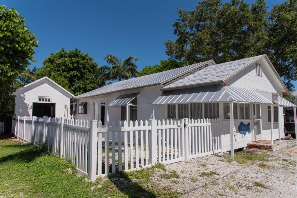 A white cottage with a metal roof and a detached garage behind a white fence — 4416 123RD ST COURT W, CORTEZ, FL