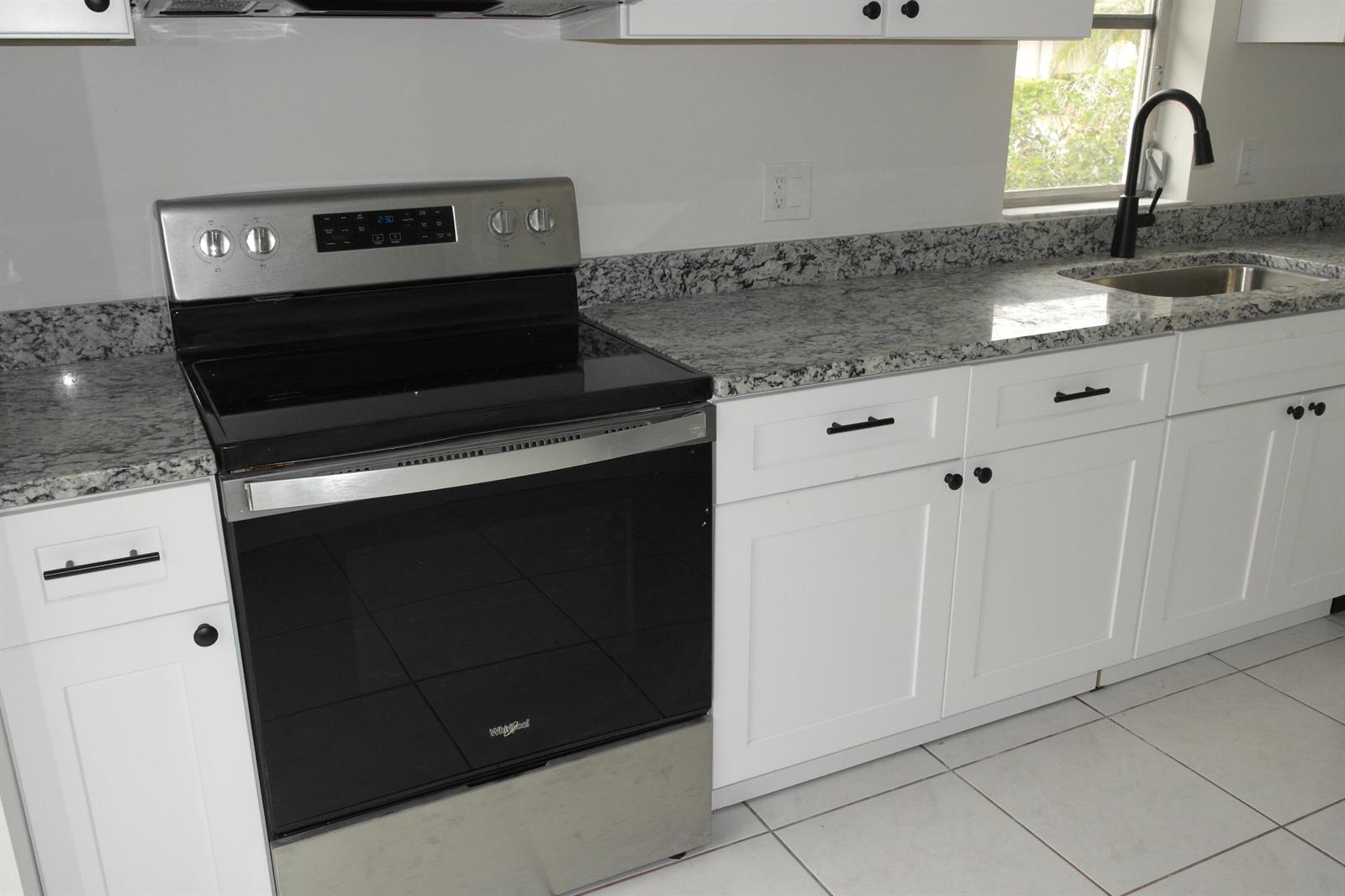 A kitchen features white cabinets, granite countertops, a stainless steel stove, and a black faucet — 18890 Candlewick Drive # B, Boca Raton FL 33496, BOCA RATON, FL