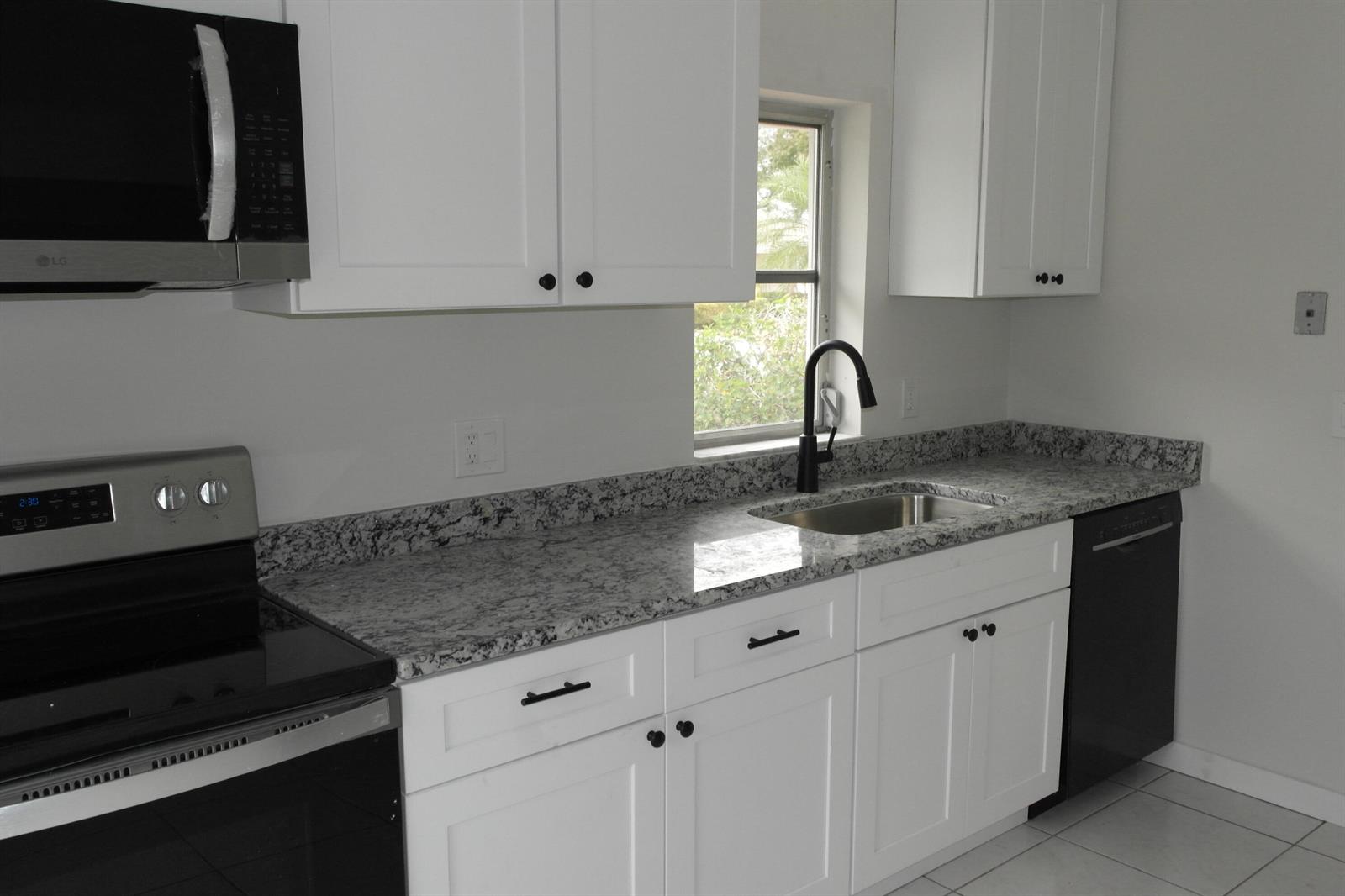 A kitchen features white cabinets, granite countertops, a stainless steel sink, and black appliances — 18890 Candlewick Drive # B, Boca Raton FL 33496, BOCA RATON, FL