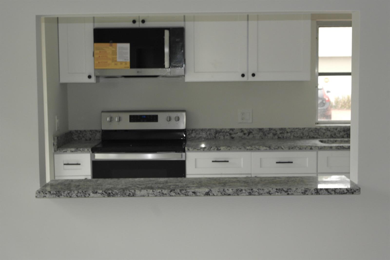 A kitchen with white cabinets, granite countertops, and stainless steel appliances viewed through a pass-through — 18890 Candlewick Drive # B, Boca Raton FL 33496, BOCA RATON, FL