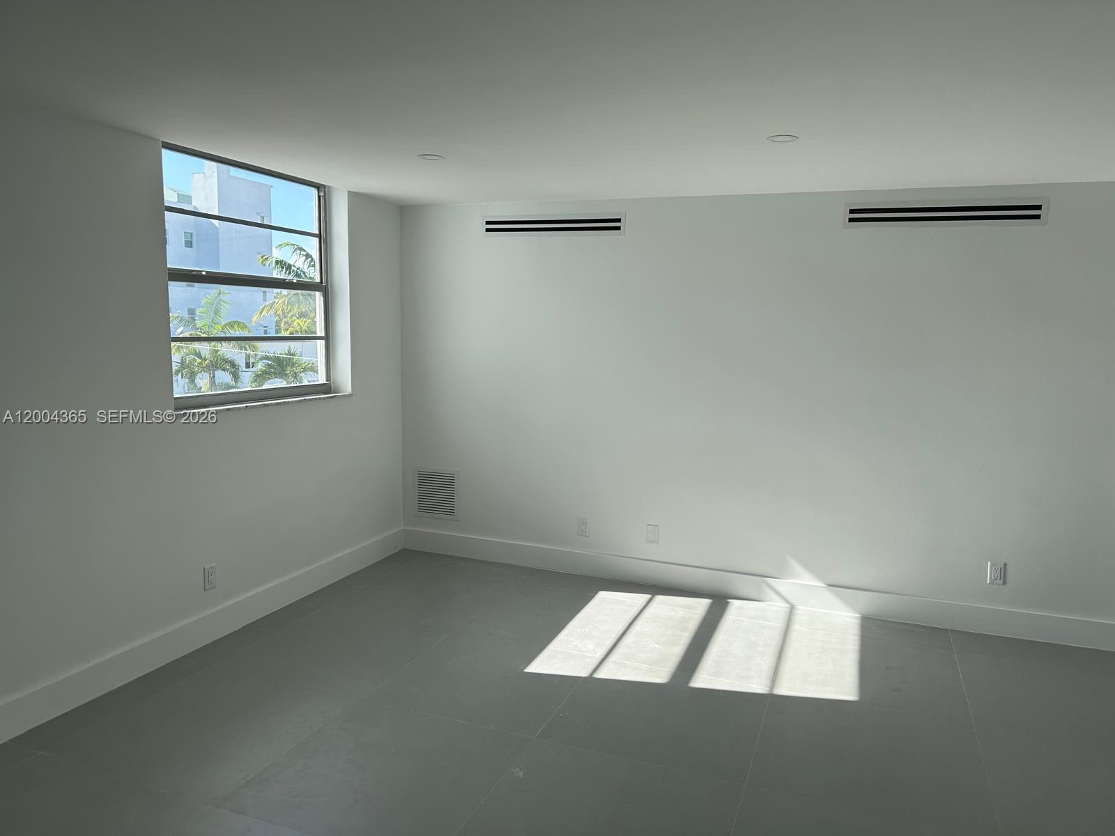 An empty room features white walls, gray tile flooring, and a window with palm trees — 360 Meridian Ave # 3E, Miami Beach FL 33139, MIAMI BEACH, FL