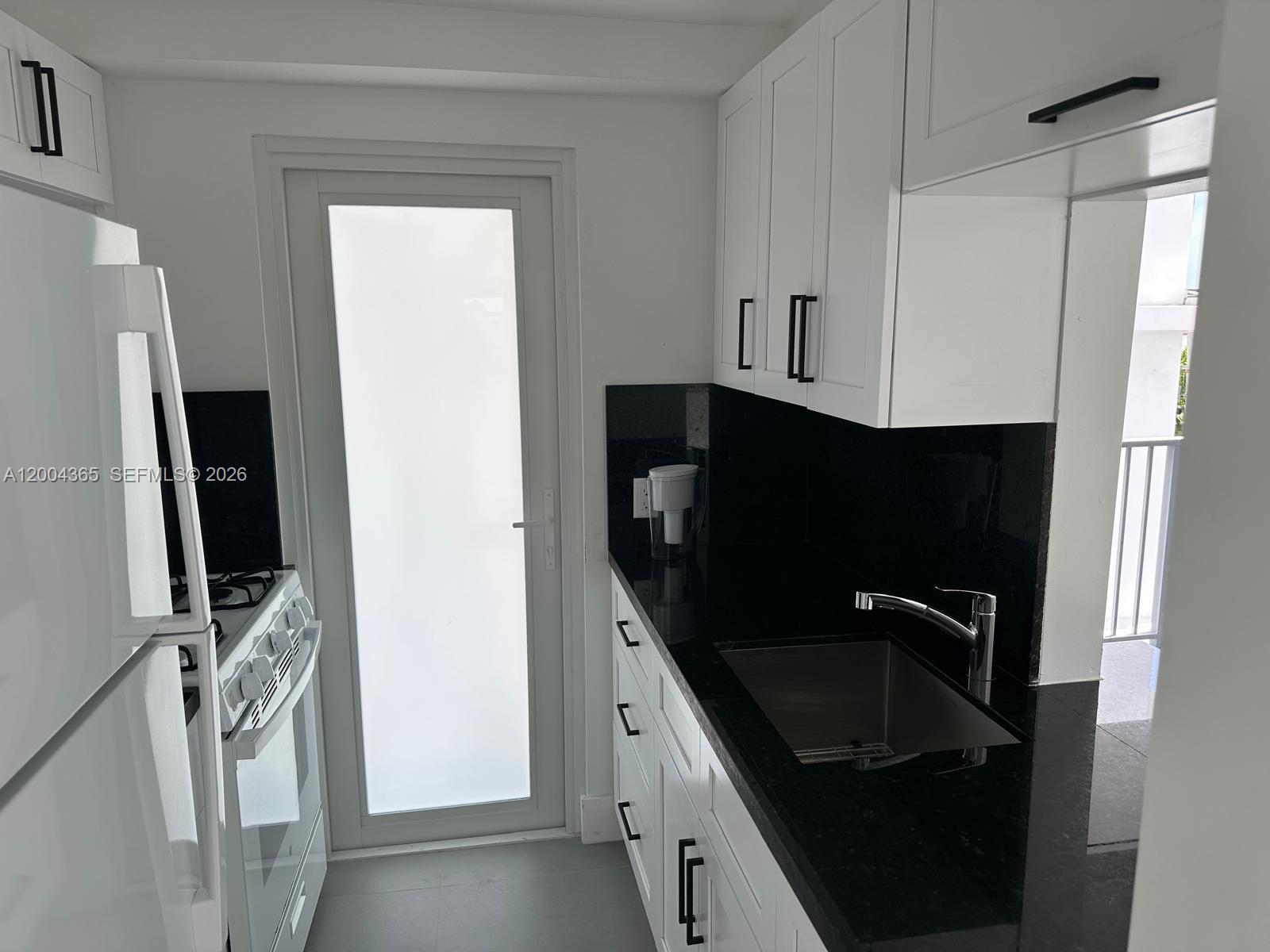 A galley kitchen features white cabinets, black countertops, a stainless steel sink, and a door — 360 Meridian Ave # 3E, Miami Beach FL 33139, MIAMI BEACH, FL