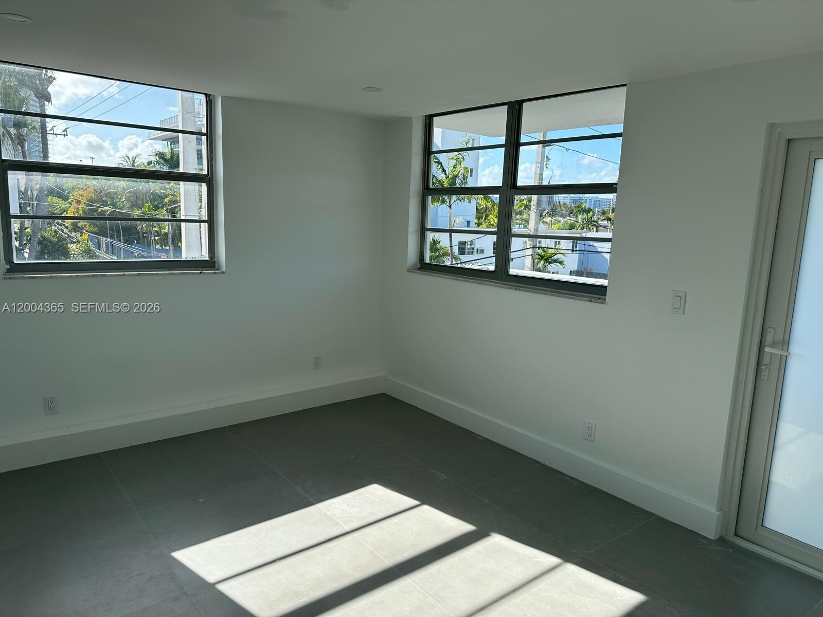 An empty room with white walls, gray tile flooring, and two windows overlooking palm trees — 360 Meridian Ave # 3E, Miami Beach FL 33139, MIAMI BEACH, FL