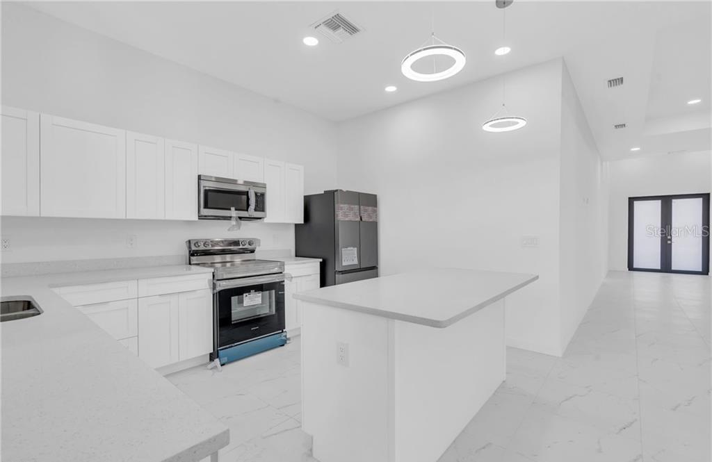 A modern kitchen features white cabinets, stainless steel appliances, a center island, and tile flooring — 3101 NW 42ND PLACE, CAPE CORAL, FL