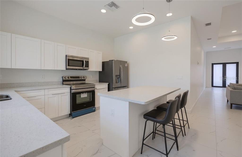 A modern kitchen features white cabinetry, stainless steel appliances, a center island, and tile flooring — 3101 NW 42ND PLACE, CAPE CORAL, FL