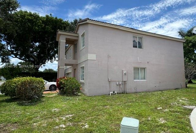 The exterior side view of a two-story stucco house features a small bush and lawn — 10275 SW 24th St, Miramar FL 33025, MIRAMAR, FL