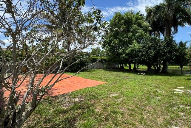 A grassy backyard features a red-tiled patio area and several mature trees — 10275 SW 24th St, Miramar FL 33025, MIRAMAR, FL