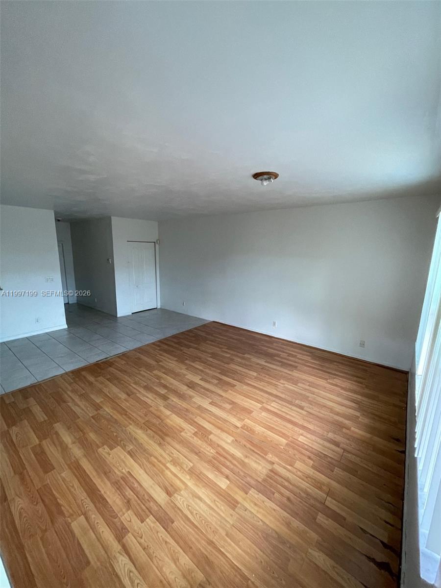 An empty living room features wood-look flooring, white walls, and a tiled entryway — 870 NE 212th Ter # 3, Miami FL 33179, MIAMI, FL