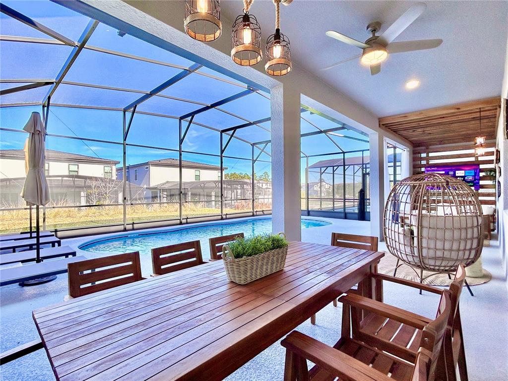 A covered patio features a wooden dining table, a hanging chair, and a screened-in pool — 6271 SAND SKIPPER ROAD, ORLANDO, FL