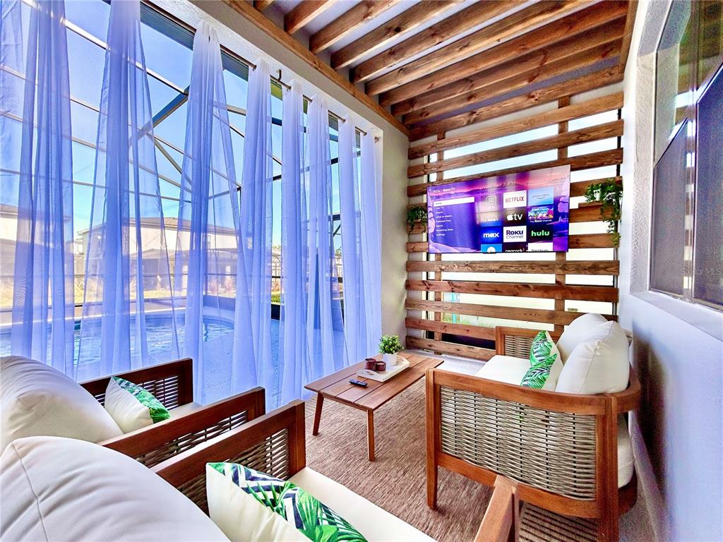 A sunroom features a wood-slat wall with a mounted television, wicker furniture, and pool views — 6271 SAND SKIPPER ROAD, ORLANDO, FL