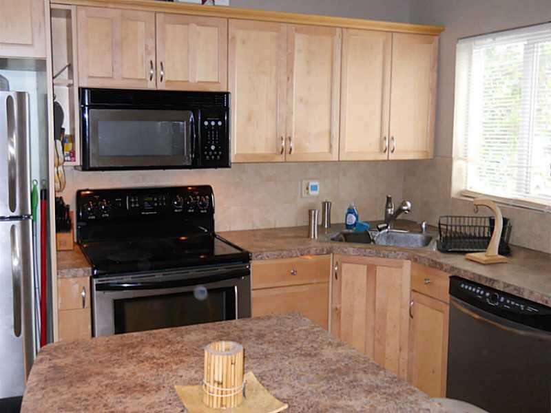 A kitchen features light wood cabinets, a black stove, a microwave, and a stone countertop — 520 SW 15th Street # 101, Pompano Beach FL 33060, POMPANO BEACH, FL
