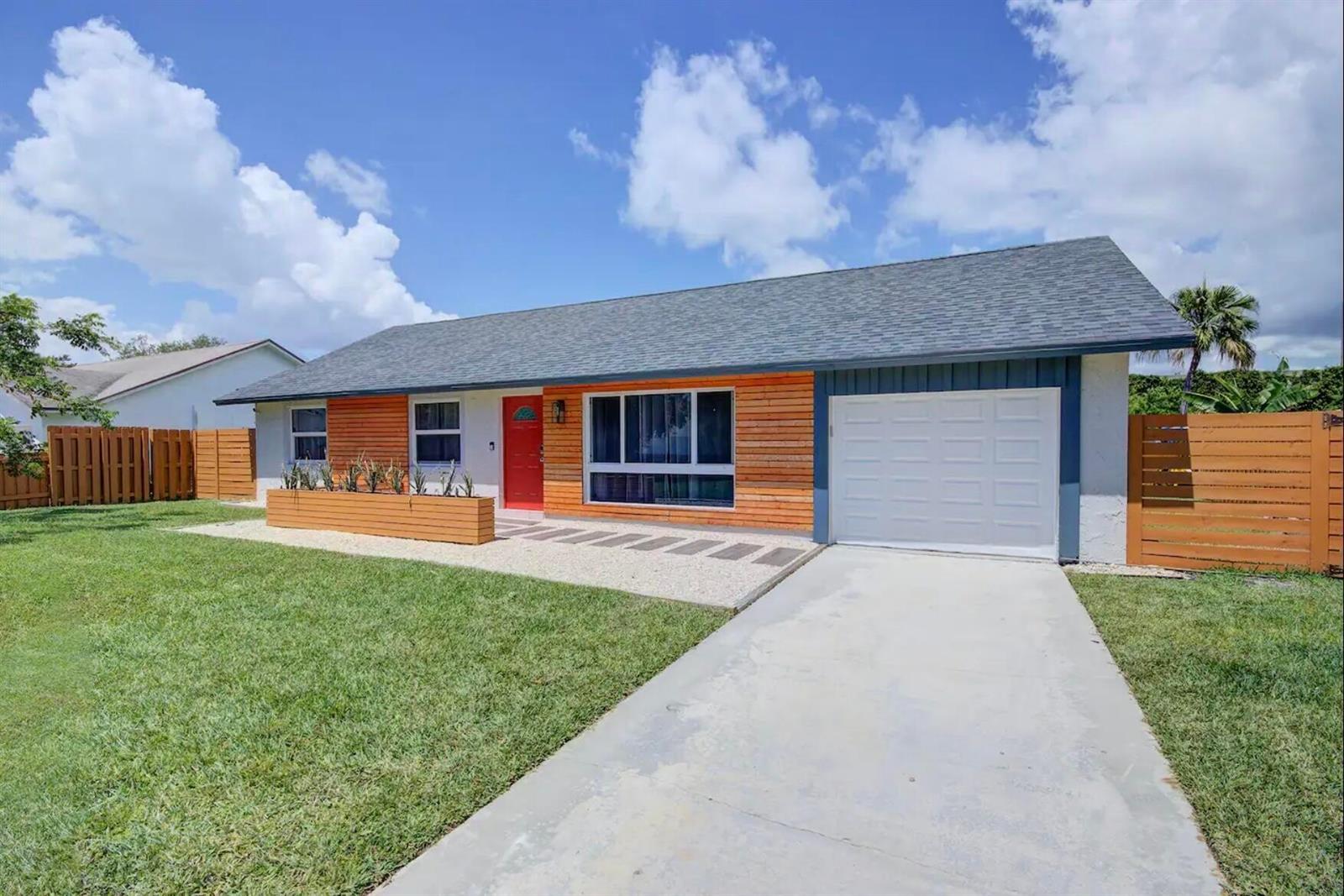 A single-story house with wood siding, a red front door, and a concrete driveway — 3026 Dunlin Road, Delray Beach FL 33444, DELRAY BEACH, FL