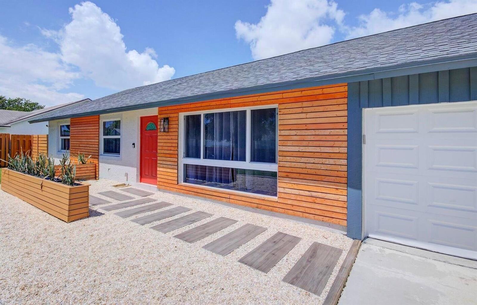 A single-story house exterior features horizontal wood siding, a red front door, and gravel landscaping — 3026 Dunlin Road, Delray Beach FL 33444, DELRAY BEACH, FL