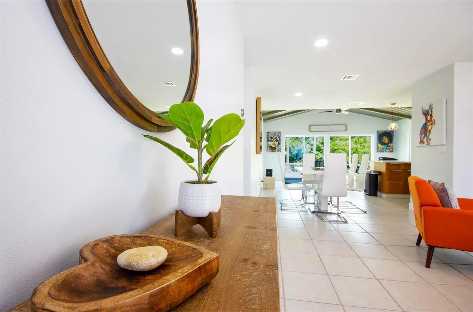 A wooden console table with a plant and mirror leads into a bright, open-concept living area — 3026 Dunlin Road, Delray Beach FL 33444, DELRAY BEACH, FL