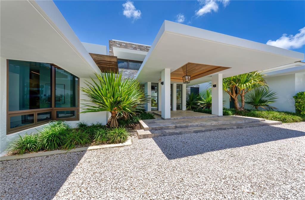 A modern house exterior features a white cantilevered entryway, stone accents, and a gravel driveway — 7000 BAHIA BEACH BLVD., 23 LAS ESTANCIAS, RIO GRANDE, PR