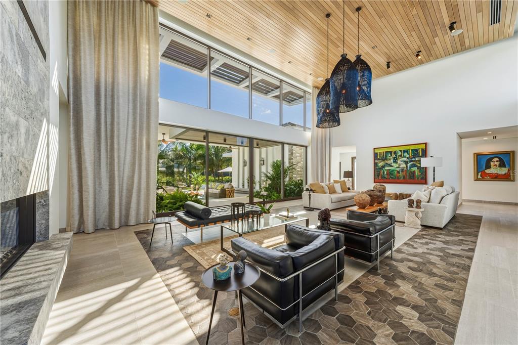 A spacious living room features a double-height ceiling, floor-to-ceiling windows, and a stone fireplace — 7000 BAHIA BEACH BLVD., 23 LAS ESTANCIAS, RIO GRANDE, PR