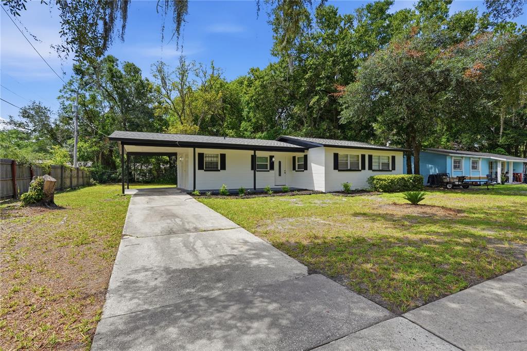 A single-story white house with a carport and a concrete driveway sits on a lawn — 1823 NE 31ST AVENUE, GAINESVILLE, FL
