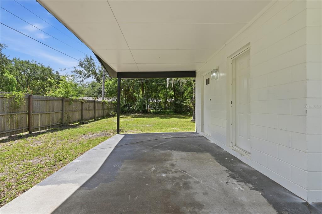 A concrete patio with a covered roof overlooks a grassy backyard enclosed by a wooden fence — 1823 NE 31ST AVENUE, GAINESVILLE, FL