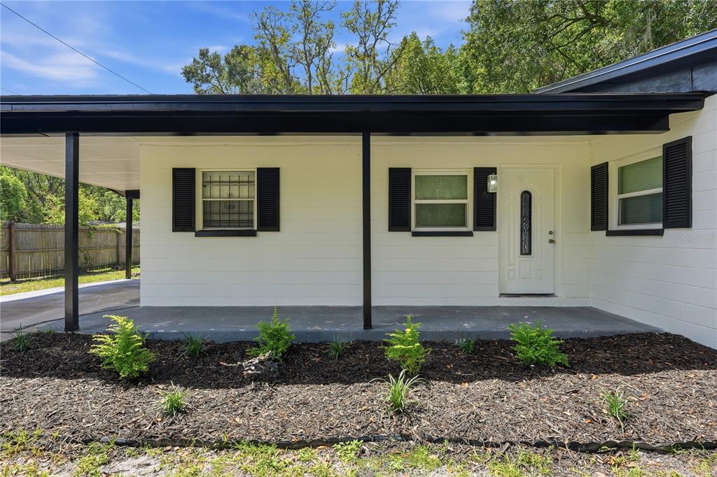 The exterior of a white, single-story house features a covered porch, black shutters, and landscaping — 1823 NE 31ST AVENUE, GAINESVILLE, FL