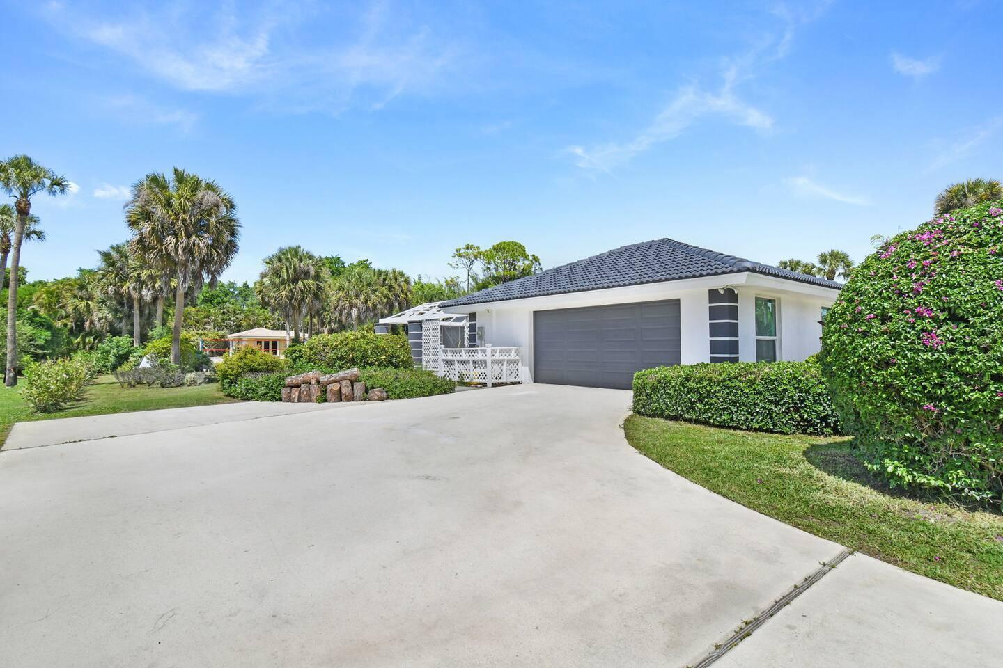 A white house with a dark roof and garage sits behind a concrete driveway — 12231 Areaca Drive, Wellington FL 33414, WELLINGTON, FL