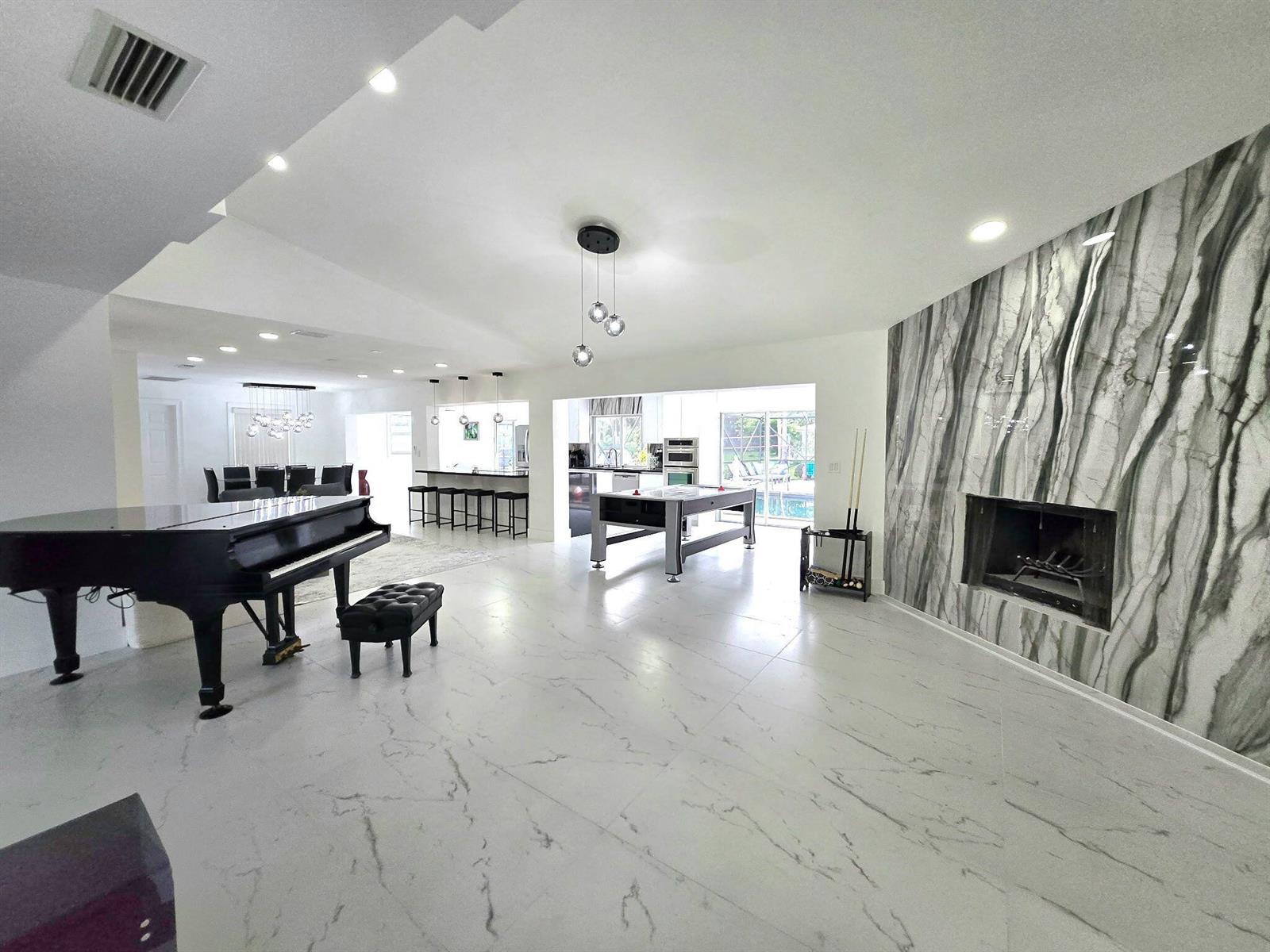 A spacious open-concept living area features a grand piano, fireplace, and marble-style flooring — 12231 Areaca Drive, Wellington FL 33414, WELLINGTON, FL