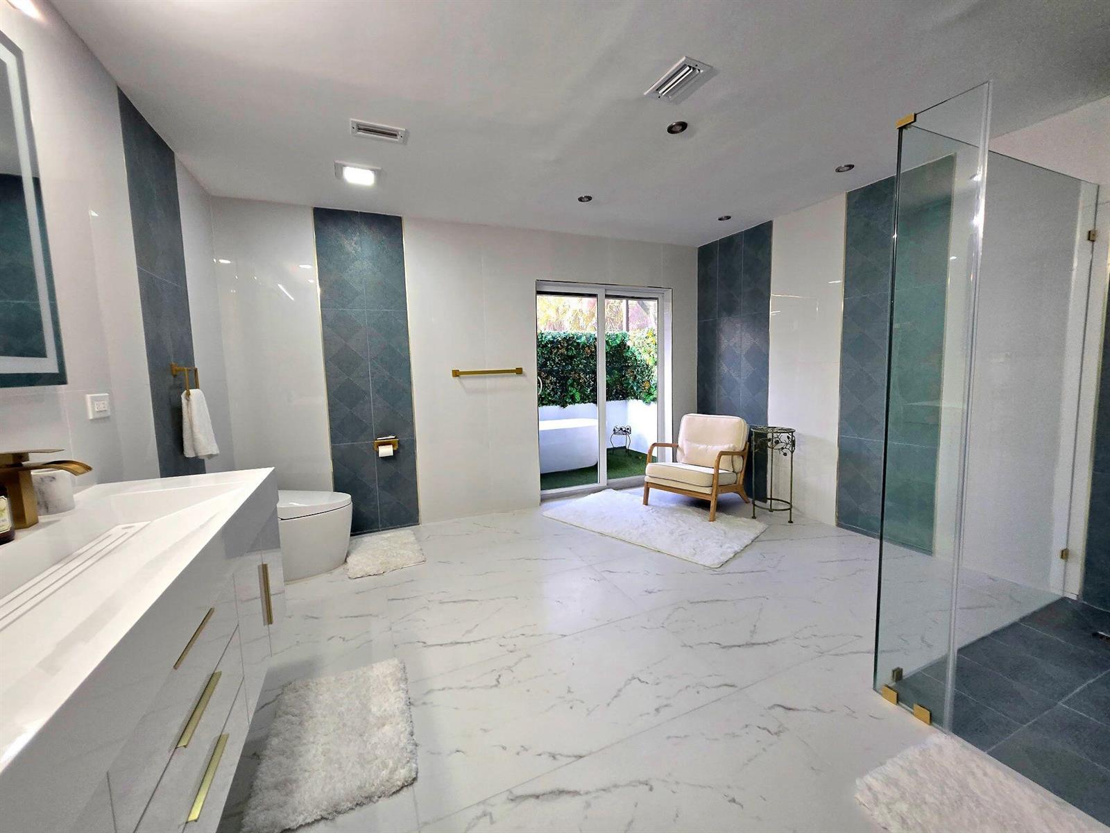 A modern bathroom features marble-look flooring, blue tiled accents, a glass shower, and a patio door — 12231 Areaca Drive, Wellington FL 33414, WELLINGTON, FL