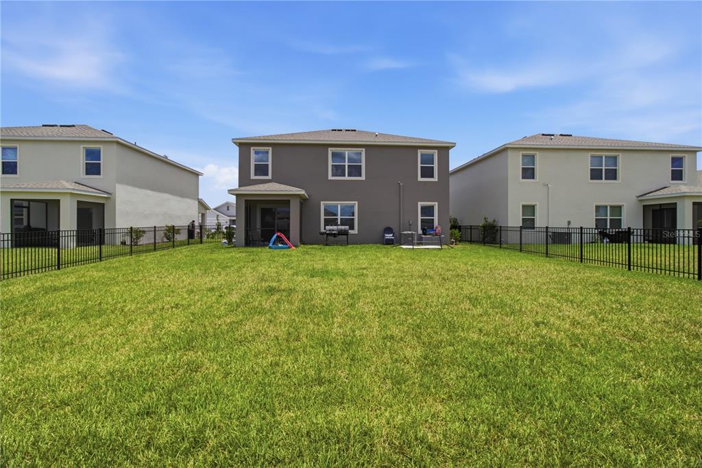 The rear exterior of a two-story house with a fenced backyard and green lawn — 18114 WHEATHOUSE PLACE, BRADENTON, FL
