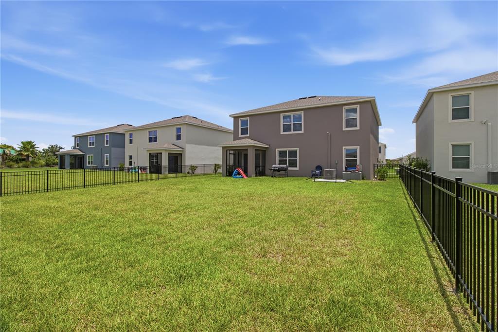The backyard of a two-story house features a screened patio and a black metal fence — 18114 WHEATHOUSE PLACE, BRADENTON, FL